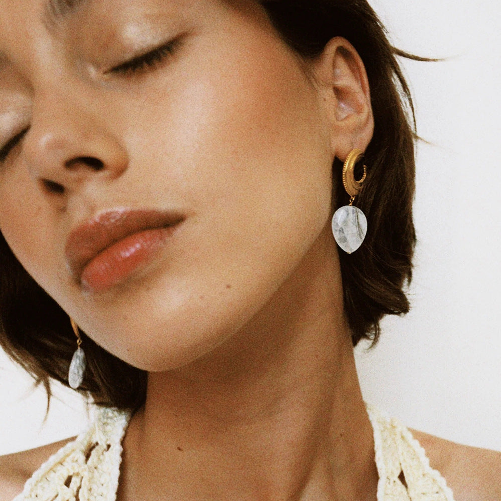 Photo of a woman wearing drop earrings in white and gold with pearl